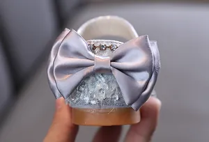 Close-up detail of silver girl's princess shoe with large satin bow and rhinestones