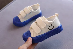 Weiße Kinder-Segeltuchschuhe mit blauer Gummisohle und Smiley-Detail für Kleinkinder.