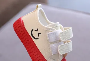 Detailansicht eines Kinder-Stoffschuhs mit Smiley-Aufdruck und roter Gummisohle