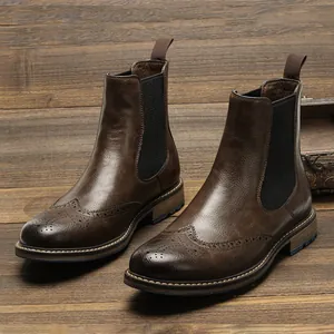 Vintage brown men's Chelsea boots with elegant brogue wingtip detailing on wooden floor.