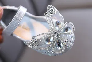 Primer plano de zapato plateado brillante para niña con detalle de mariposa de strass