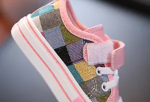 Close-up of children's low-top canvas shoe with colorful plaid fabric and pink trim.