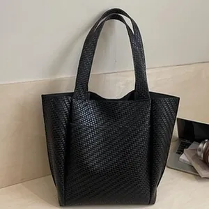 Vista detallada de un bolso tote negro para mujer con tejido de burbujas en un escritorio moderno.