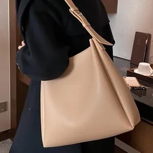 Primer plano lateral de un bolso hobo minimalista beige con un elegante abrigo oscuro