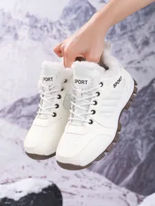 Close-up of white faux fur-lined snow boots held against a snowy mountain background