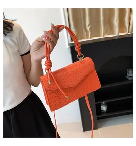 Dettaglio di una borsa a mano quadrata arancione plissettata con manico annodato