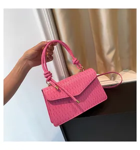 Dettaglio di borsa a mano rosa plissettata con manico annodato e chiusura a patta