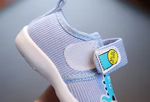 Détail de chaussures souples bleues pour bébé avec tissu rayé et fermeture par velcro.