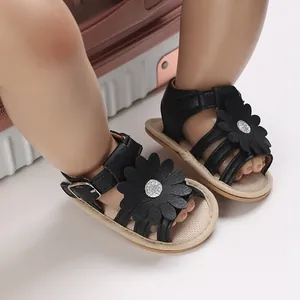 Detailansicht von schwarzen Babysandalen mit großer 3D-Blume und Glitzermitte an Babyfüßen.