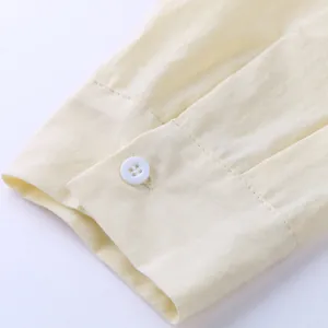 Detail of light yellow linen shirt cuff with a white button and neat stitching.