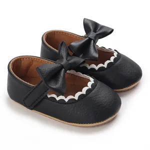 Detailed close-up of black baby princess shoes with leather bow and scalloped trim