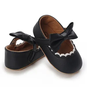Close-up of black baby girl walking shoes featuring a large bow and white scalloped trim