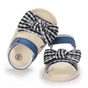 Dettaglio di sandali per neonata con fiocchi a quadretti neri e cinturini in denim.