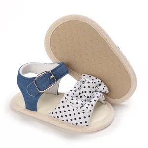 Dettaglio di sandali per neonata con cinturino in denim blu e fiocco a pois neri