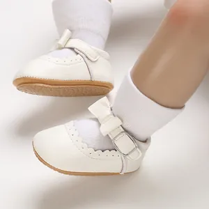 Close-up of white soft-soled baby princess shoes with bow and scalloped edge detail