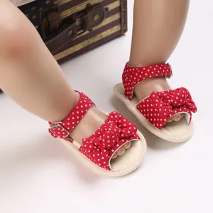 Dettaglio dei sandali estivi rossi a pois per neonata con fiocco decorativo.