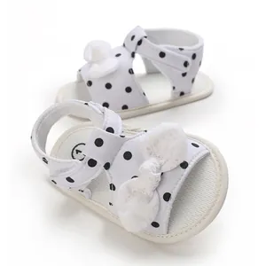 Adorable white baby sandals with black polka dots and white bow detail on white background