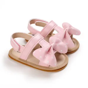 Detalle de sandalias rosas para bebé niña con lazo de lunares y suela blanda de verano