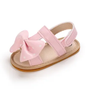 Primer plano de sandalias rosas para bebés niñas con lazo de lunares y suela blanda cómoda.