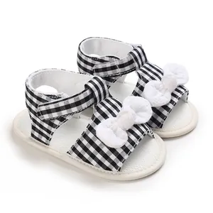 Close-up of baby sandals featuring black and white checkered pattern with white bows
