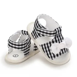 Close-up of black and white gingham baby girl sandals decorated with a soft white bow