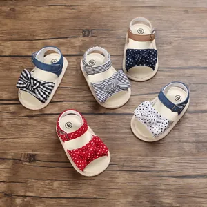 Selezione di sandali per neonata con fiocchi e fantasie varie su fondo in legno