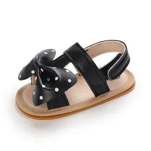 Detalle de sandalias negras para bebé niña con un lazo de lunares y suela flexible.