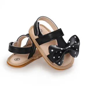 Detalle de sandalias negras para bebé niña con lazo de lunares y suela blanda color canela.