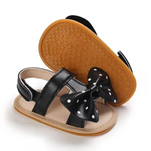 Detalle de sandalias negras para bebé con lazo de lunares y suela blanda flexible