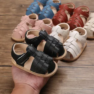 Hand holding black leather baby sandals with woven straps and soft non-slip sole