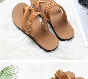 Close-up detail of women's tan flat beach sandals with hollow woven straps on white rug.