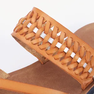 Detailed view of woven tan leather sandal strap with silver accent on white background
