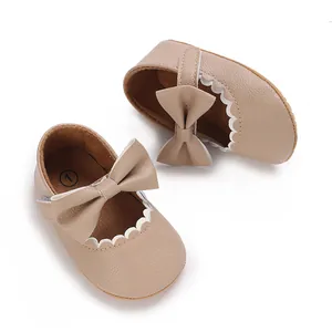 Macro view of beige synthetic leather baby Mary Jane shoes featuring bow and scalloped trim