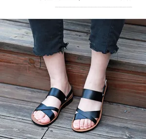 Vue détaillée de sandales plates noires pour femmes avec brides croisées sur bois.
