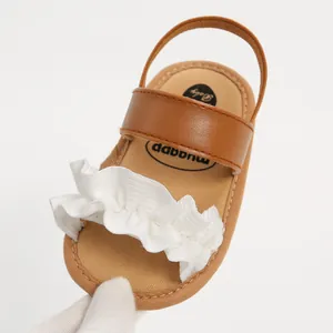 Detailansicht brauner Babysandalen für Mädchen mit weißen Rüschen und weicher Sohle.