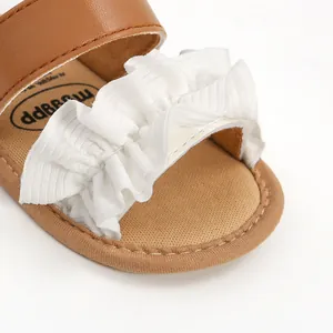 Nahaufnahme des weißen Rüschenbesatzes an einer braunen Baby-Sommersandale aus Leder