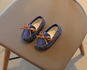 Close-up of children's blue suede loafers with brown bow detail on a brown chair