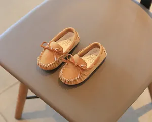 Close-up of brown suede children's loafers with bow detail on a brown chair