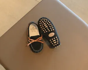 Close-up of black toddler loafers featuring a brown bow and non-slip rubber sole