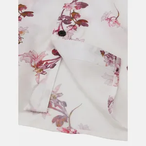 Detailed view of the soft fabric texture and button on a white floral print Hawaiian shirt.