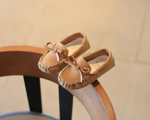 Close-up detail of brown suede kids moccasin shoes featuring a bow tie on a wooden chair