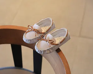 Close-up of toddler suede moccasins with tan leather bow detail on a wooden chair
