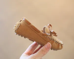 Close-up of brown suede children's loafers with a decorative bow and white stitching.