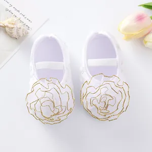 Close-up of white baby princess shoes with gold-trimmed flower decor and soft sole