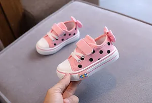 Close-up of pink toddler canvas shoes with black polka dots and a decorative heel bow.