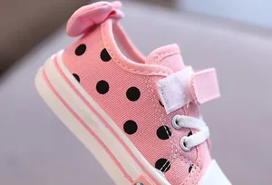 Close-up of pink children's canvas shoe with black polka dots and cute heel bow