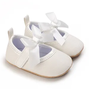 Close-up detail of white glittery baby girl princess shoes with a large satin ribbon bow