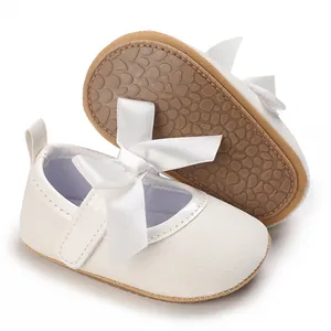 Close-up of white glitter baby shoes with non-slip rubber sole and satin bow.