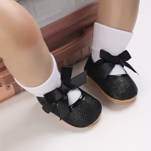 Detailed view of black glitter baby princess shoes with elegant satin bows and white socks.