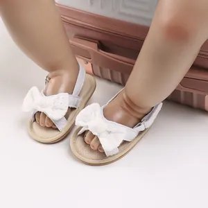 Detailed view of white infant walking sandals with elegant lace bow on doll feet